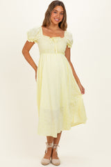 woman wearing a light yellow maternity dress with short puff sleeves and a smocked bodice, showcasing her baby bump