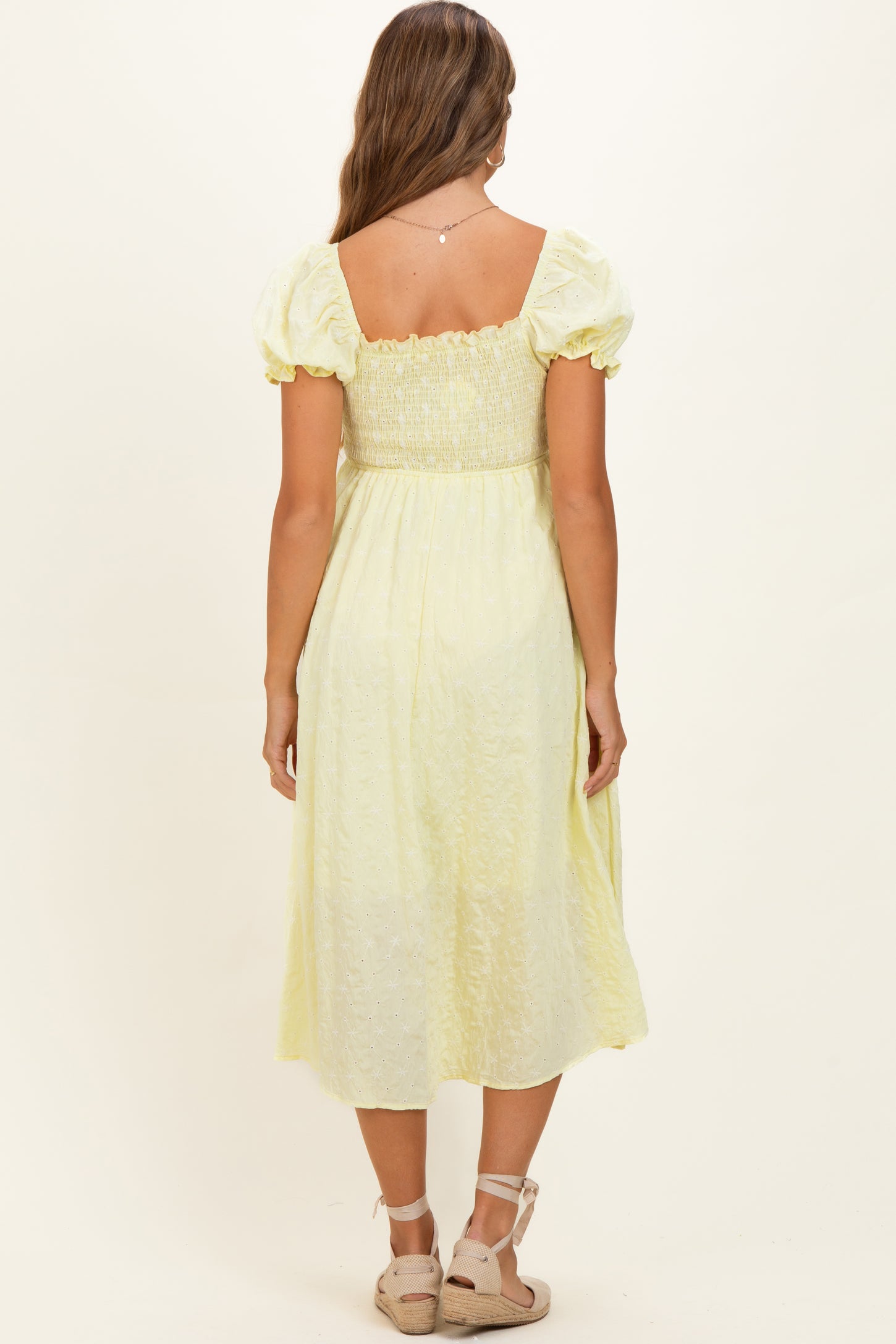 woman wearing a light yellow maternity dress with a smocked bodice and puff sleeves, viewed from the back