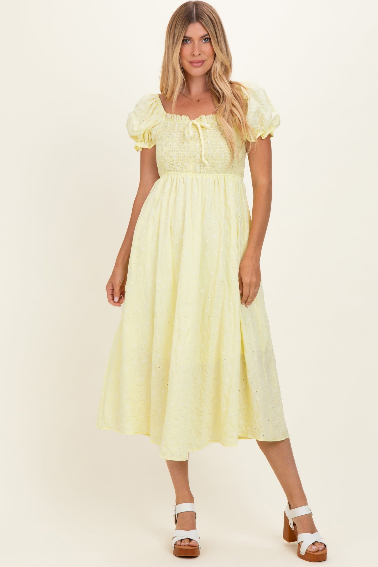 woman wearing a light yellow midi dress with puff sleeves and tie detail at the neckline