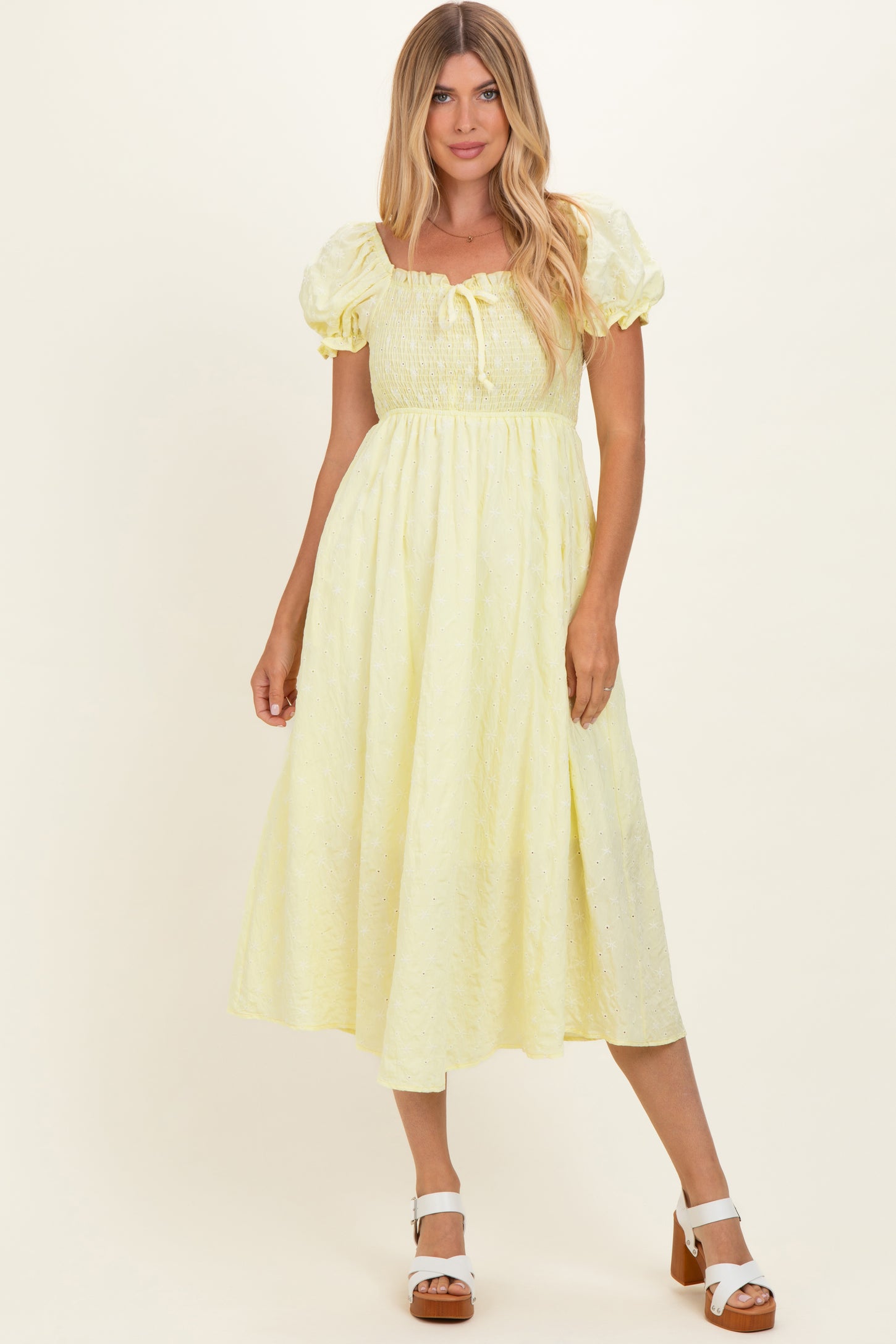 woman wearing a light yellow midi dress with puff sleeves and tie detail at the neckline