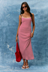 woman wearing a red and white striped maxi dress with thin straps, holding a red tote bag and wearing sunglasses