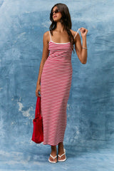 woman wearing a red and white striped maxi dress with spaghetti straps and holding a red bag