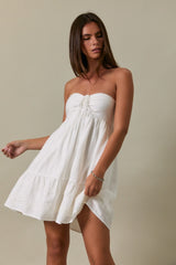 woman wearing a strapless white casual dress with a ruffled hem and a tie-front detail