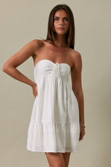 woman wearing a white strapless mini dress with a drawstring and ruffled hemline