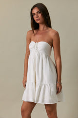 woman wearing a white strapless sundress with a ruffled hem and a front button detail