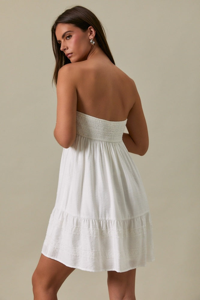 woman wearing a white strapless sundress with a smocked bodice and tiered hemline