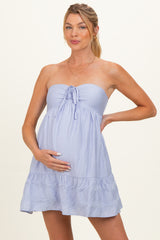 woman wearing a light lavender strapless maternity dress with a tie front and ruffled hem, cradling her baby bump