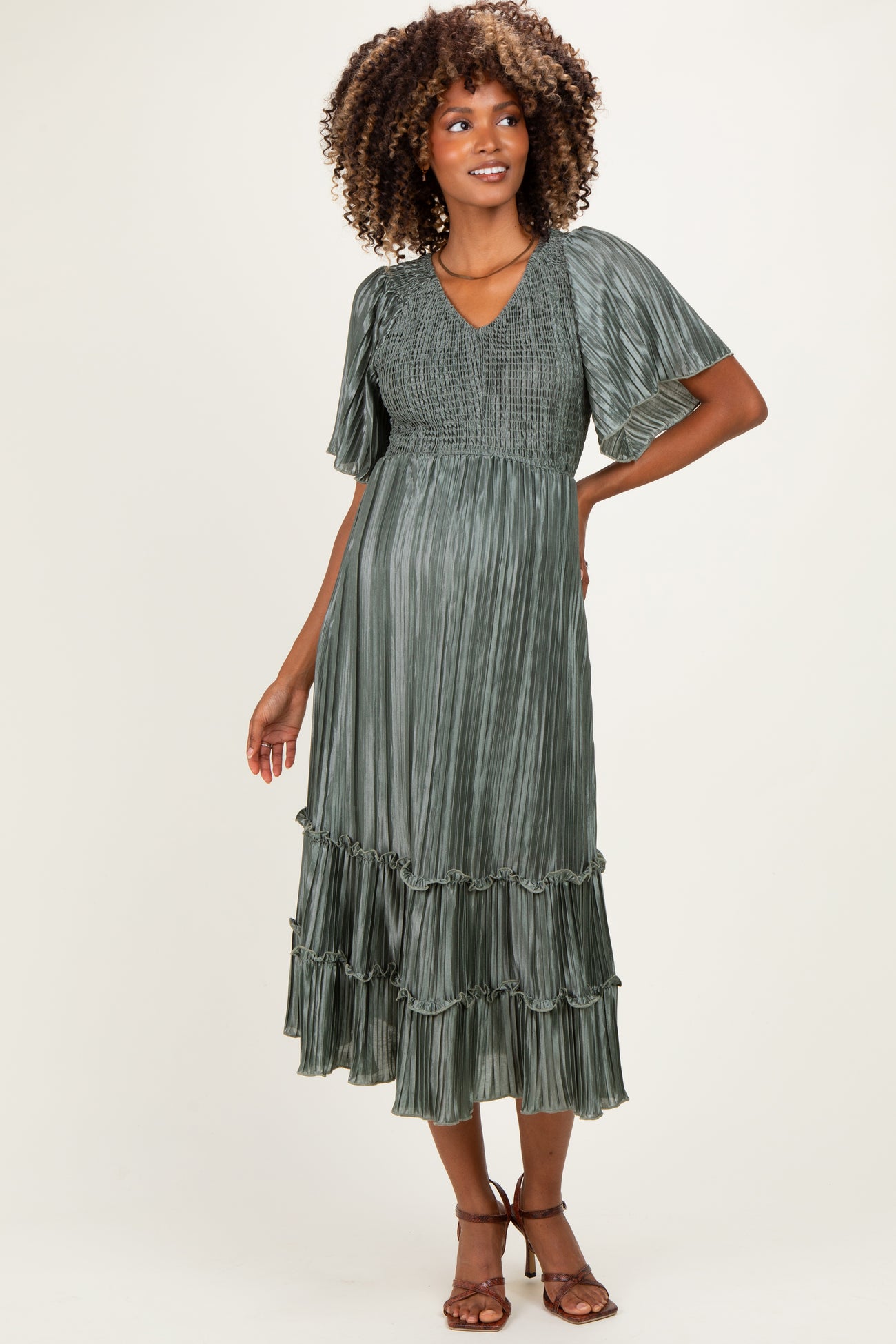 woman wearing a green pleated maternity dress with flutter sleeves and a tiered hem, showing her baby bump