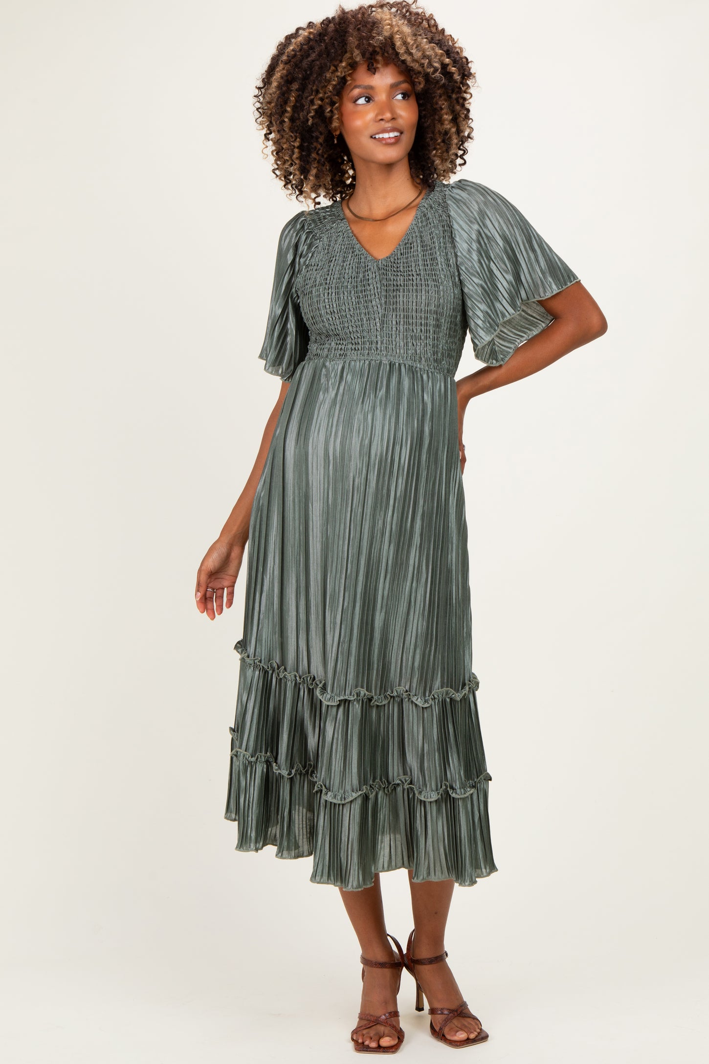 woman wearing a green pleated maternity dress with flutter sleeves and a tiered hem, showing her baby bump