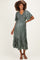 woman wearing a green pleated maternity dress with flutter sleeves and a tiered hem, showing her baby bump