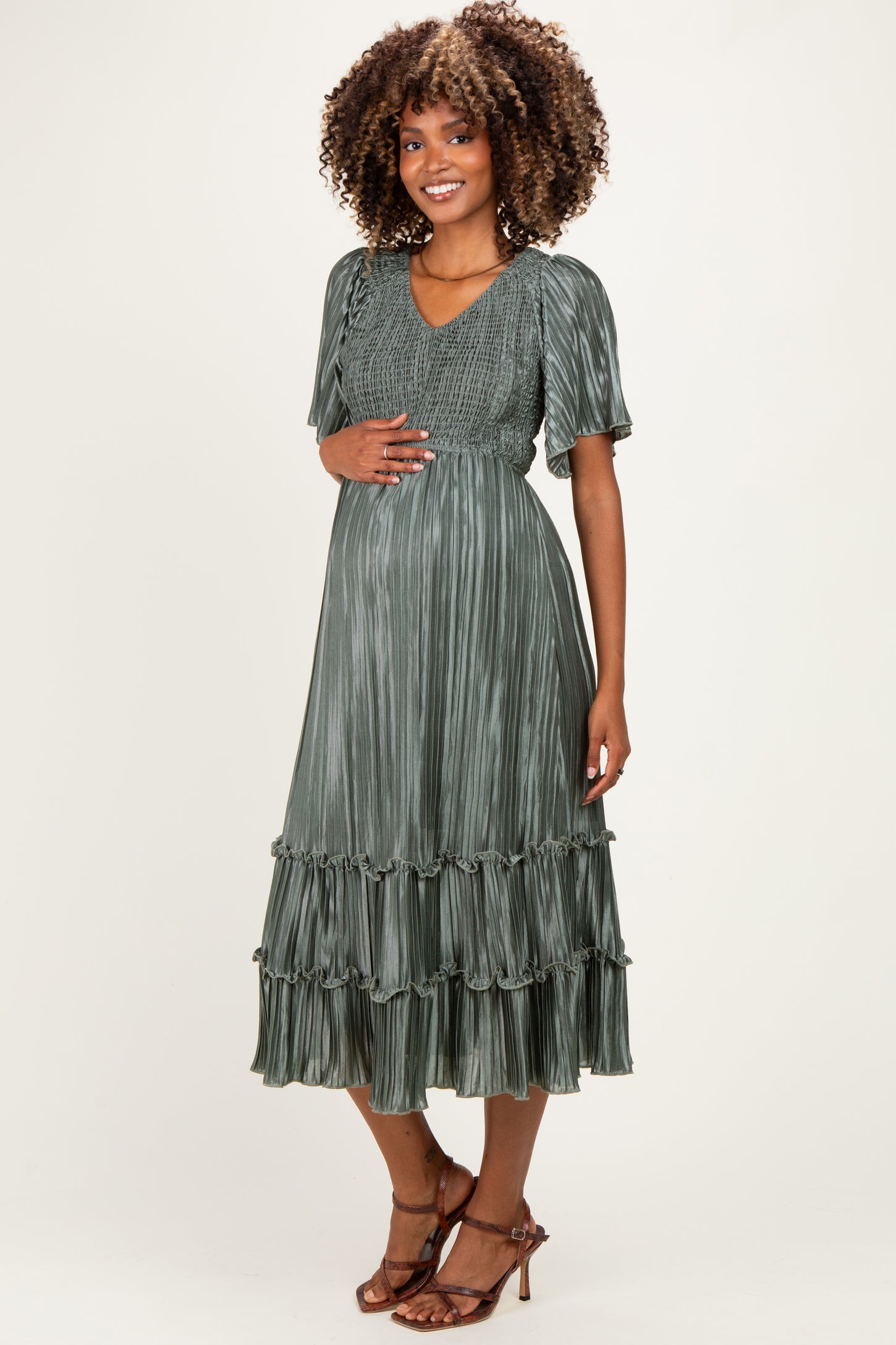 woman wearing a green pleated short sleeve maternity dress with tiered ruffles and a baby bump visible