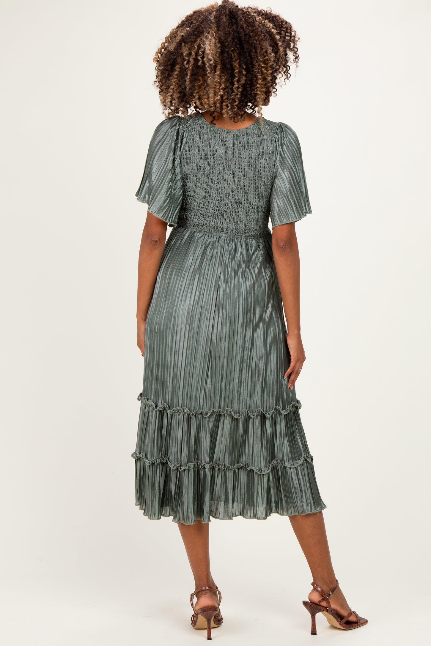 woman wearing a green maternity dress with pleated detail and ruffled hem, showing her back and curly hair