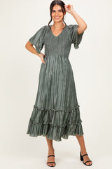 woman wearing a green pleated midi dress with short sleeves and a ruffled hem, smiling and posing with one hand raised
