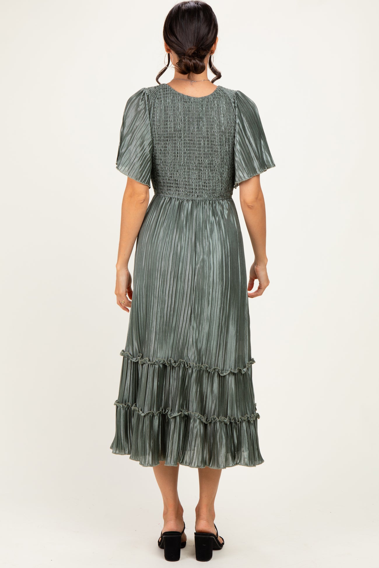 woman wearing a green pleated midi dress with short sleeves and ruffle details, seen from the back