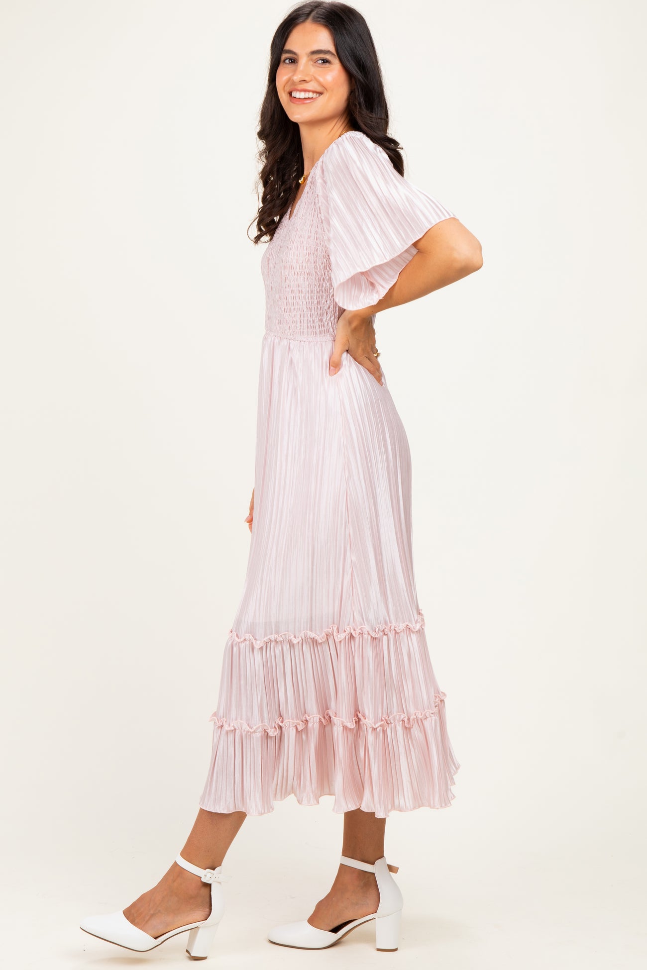 woman wearing a light pink pleated midi dress with ruffled hem and short sleeves, smiling and standing sideways
