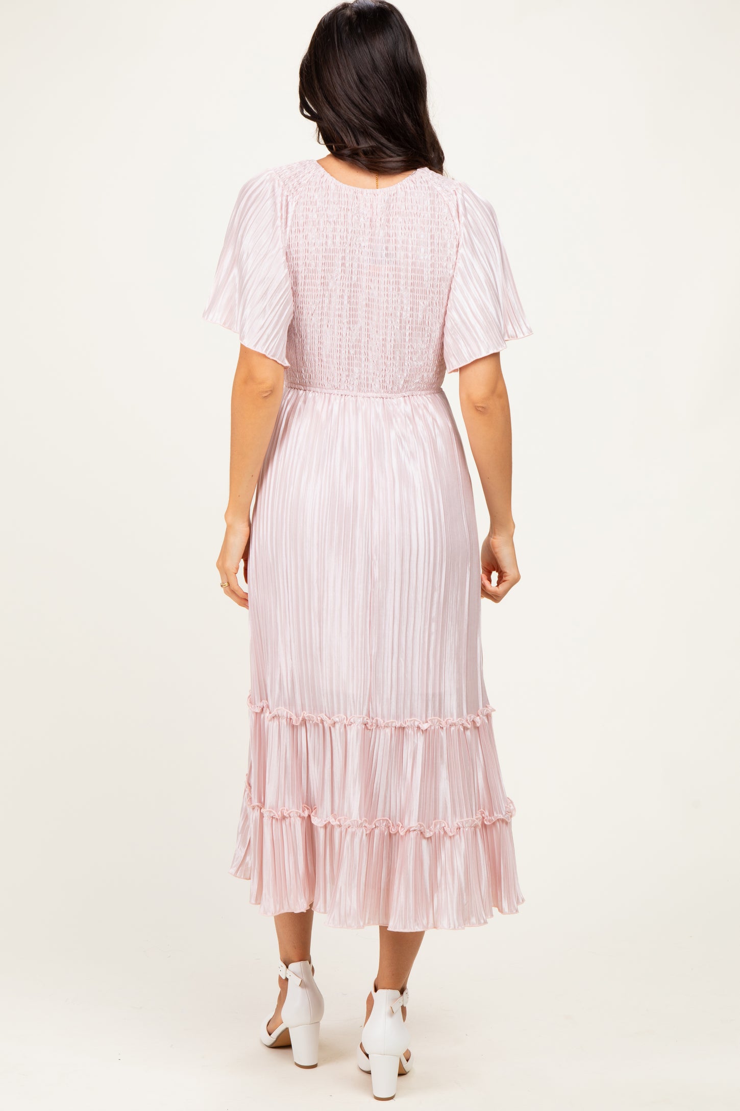 woman wearing a light pink pleated midi dress with short sleeves and ruffled hemline, viewed from the back