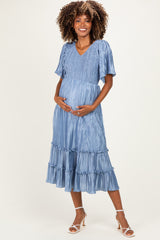 woman wearing a light blue maternity dress with a smocked bodice and ruffled hem, holding her baby bump
