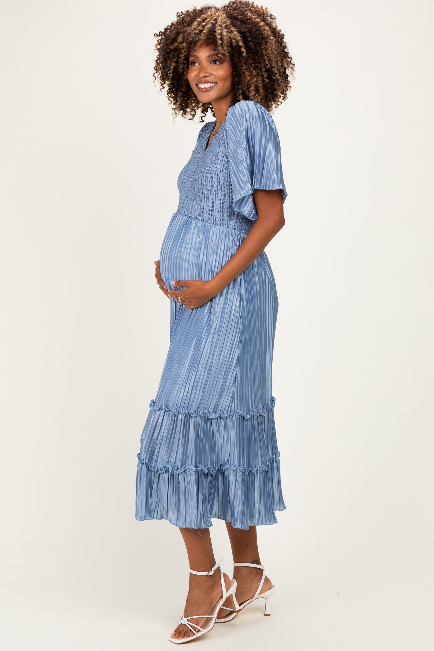 woman wearing a light blue pleated maternity dress with short sleeves and ruffle details, holding her baby bump