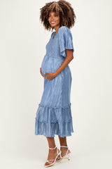 woman wearing a light blue pleated maternity dress with short sleeves and ruffle details, holding her baby bump
