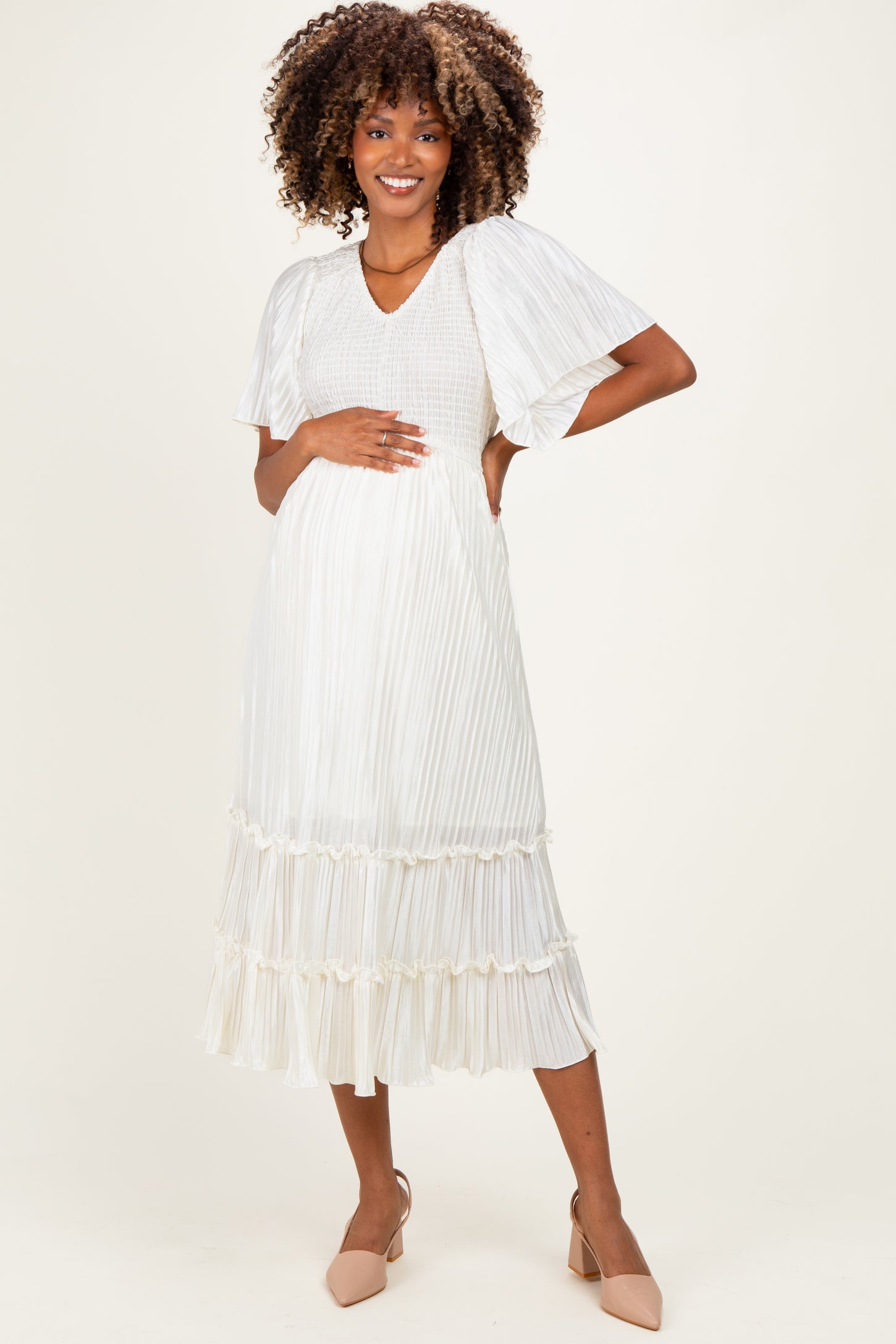 woman wearing a white pleated maternity dress with short flutter sleeves and a flowing skirt, showcasing her baby bump