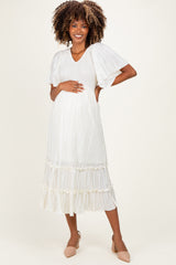 woman wearing a white pleated maternity dress with short flutter sleeves and a flowing skirt, showcasing her baby bump