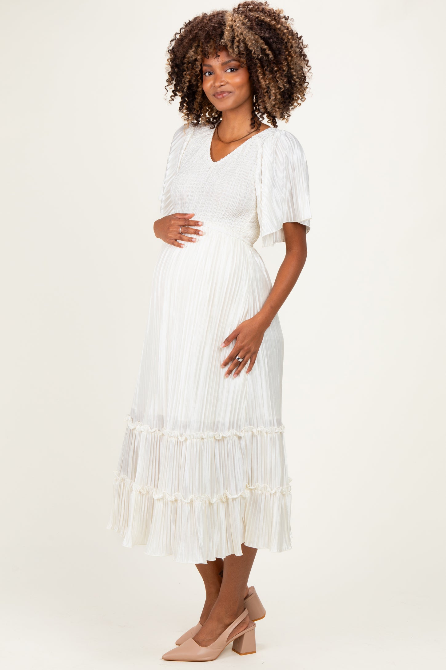woman wearing a white maternity dress with pleated details and tiered ruffles, holding her baby bump