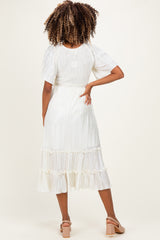 woman wearing a white pleated maternity dress with short flutter sleeves and a tiered hem, showing her baby bump