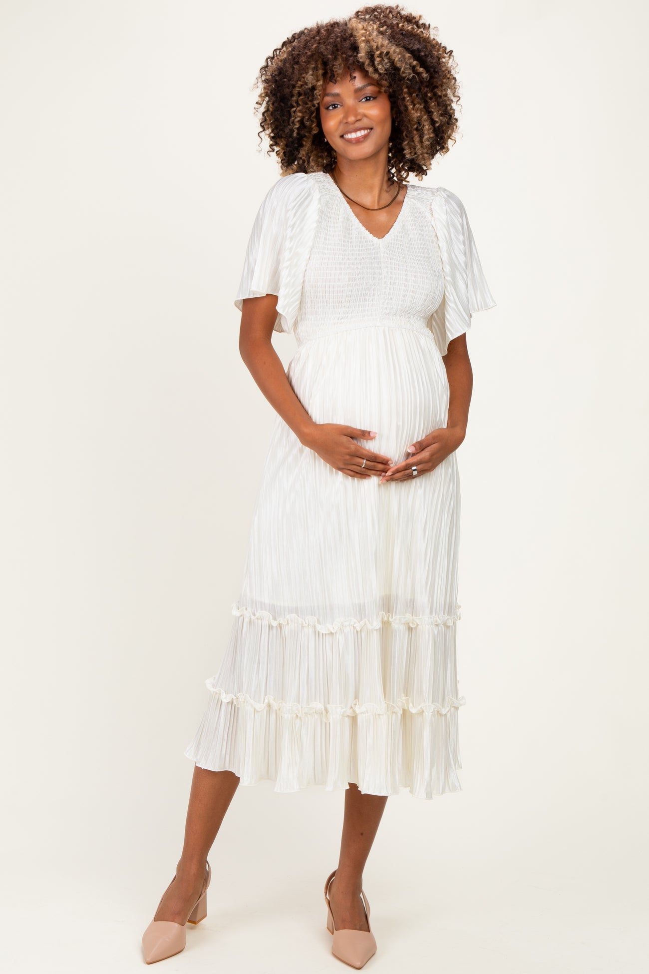 woman wearing a white maternity dress with short sleeves and tiered ruffles, cradling her baby bump