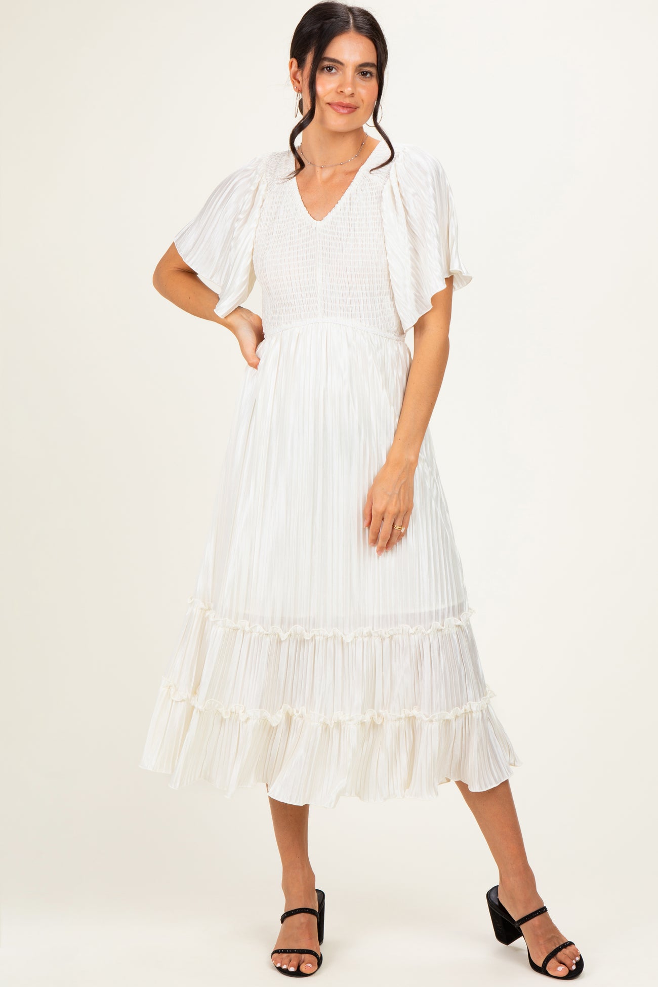 woman wearing a white pleated midi dress with flutter sleeves and ruffled hem, standing in a relaxed pose