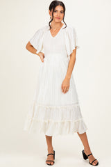 woman wearing a white pleated midi dress with flutter sleeves and ruffled hem, standing in a relaxed pose