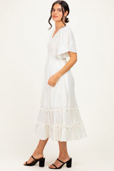 woman wearing a white pleated midi dress with flutter sleeves and ruffled hem, standing sideways with a smile