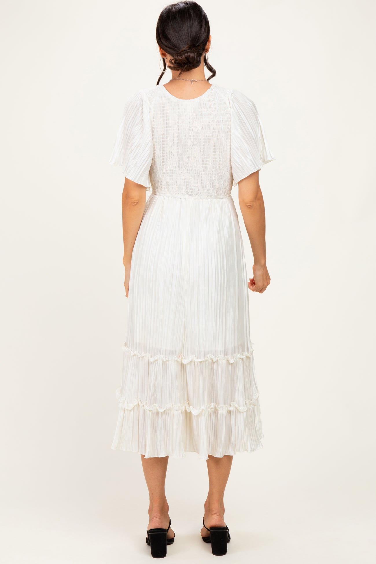 woman wearing a white pleated midi dress with short sleeves and a tiered ruffled hem, shown from the back