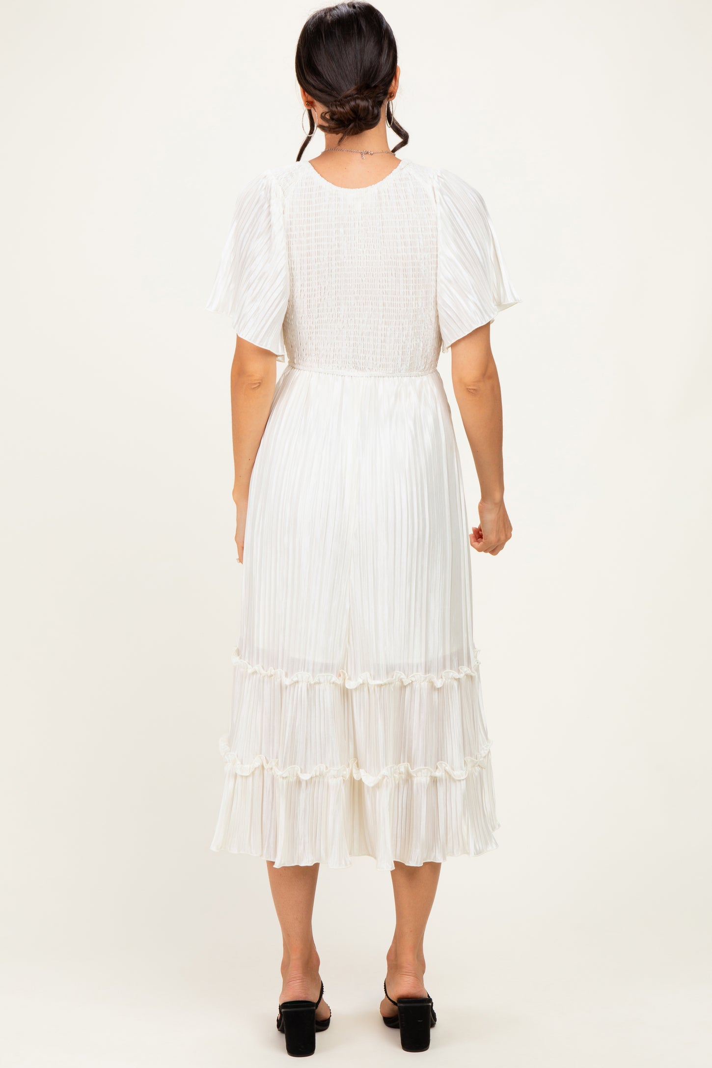 woman wearing a white pleated midi dress with short sleeves and a tiered ruffled hem, shown from the back
