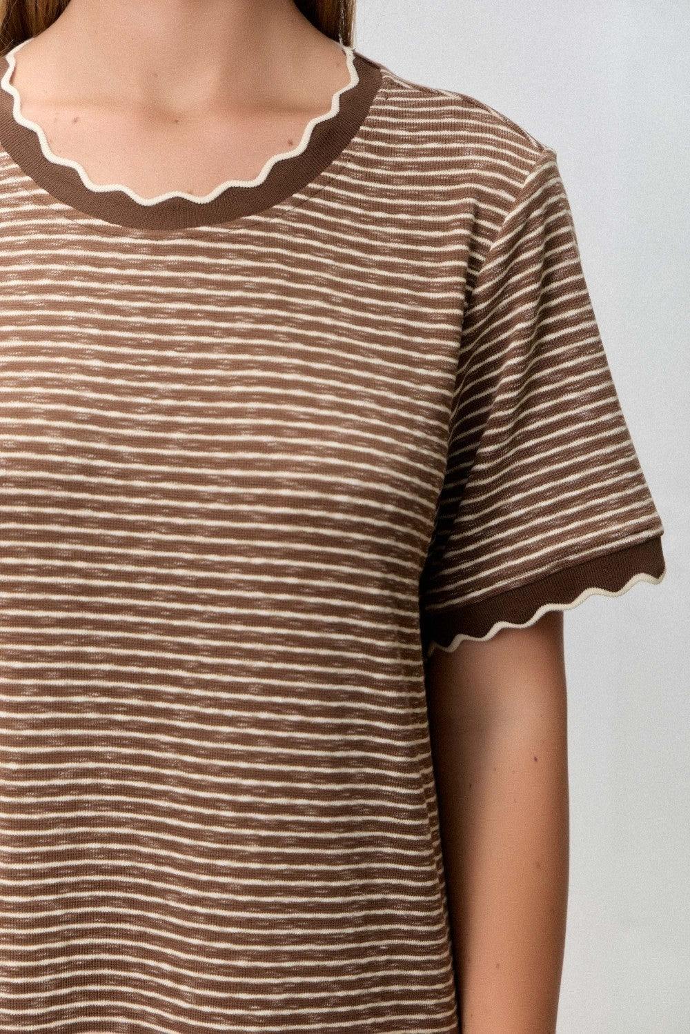 woman wearing a brown striped t-shirt with a scalloped neckline and sleeve hem