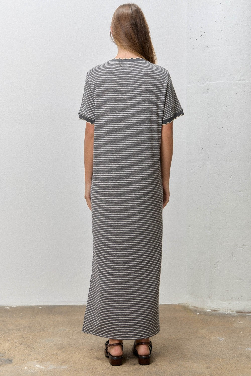 woman wearing a long striped grey maxi dress with scalloped sleeves, standing with her back to the camera