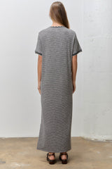 woman wearing a long striped grey maxi dress with scalloped sleeves, standing with her back to the camera