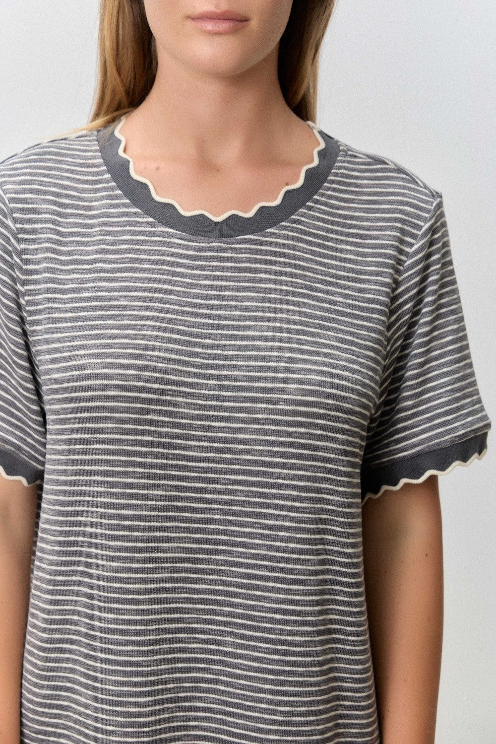 woman wearing a gray striped t-shirt with scalloped neckline and sleeve edges