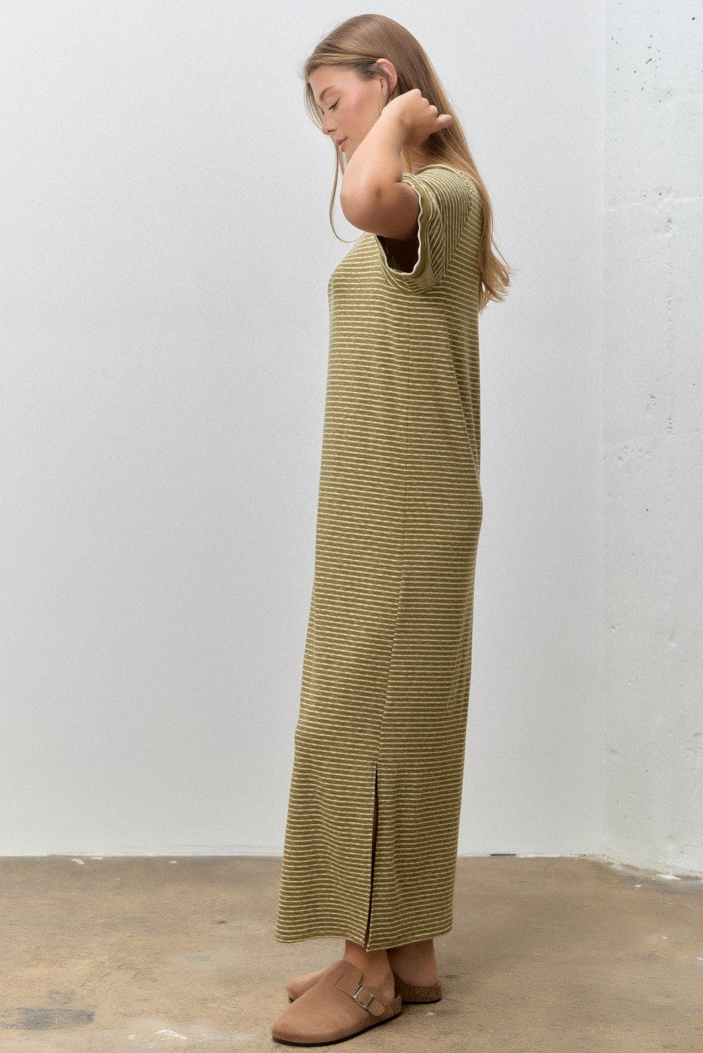 woman wearing a striped olive green maxi dress with side slits and casual brown slip-on shoes