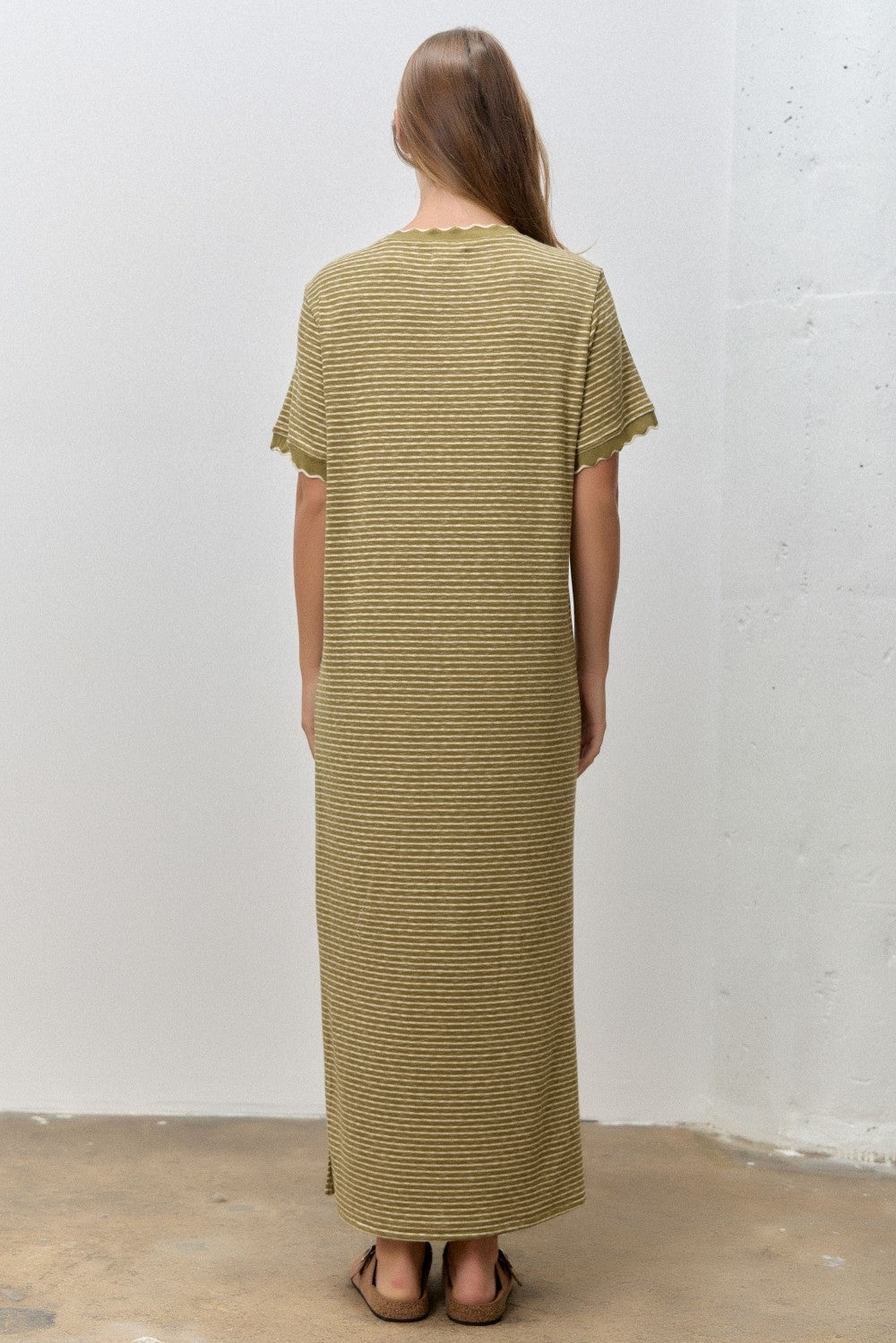 woman wearing a long olive green and beige striped maxi dress with short sleeves, viewed from the back
