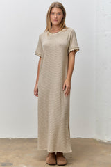 woman wearing a beige striped maxi dress with scalloped edges and side slits, standing on a concrete floor