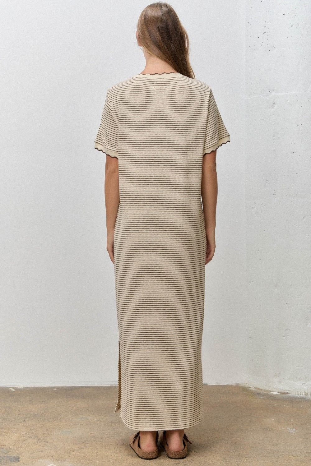 woman wearing a beige striped maxi dress with short sleeves and side slits, viewed from the back