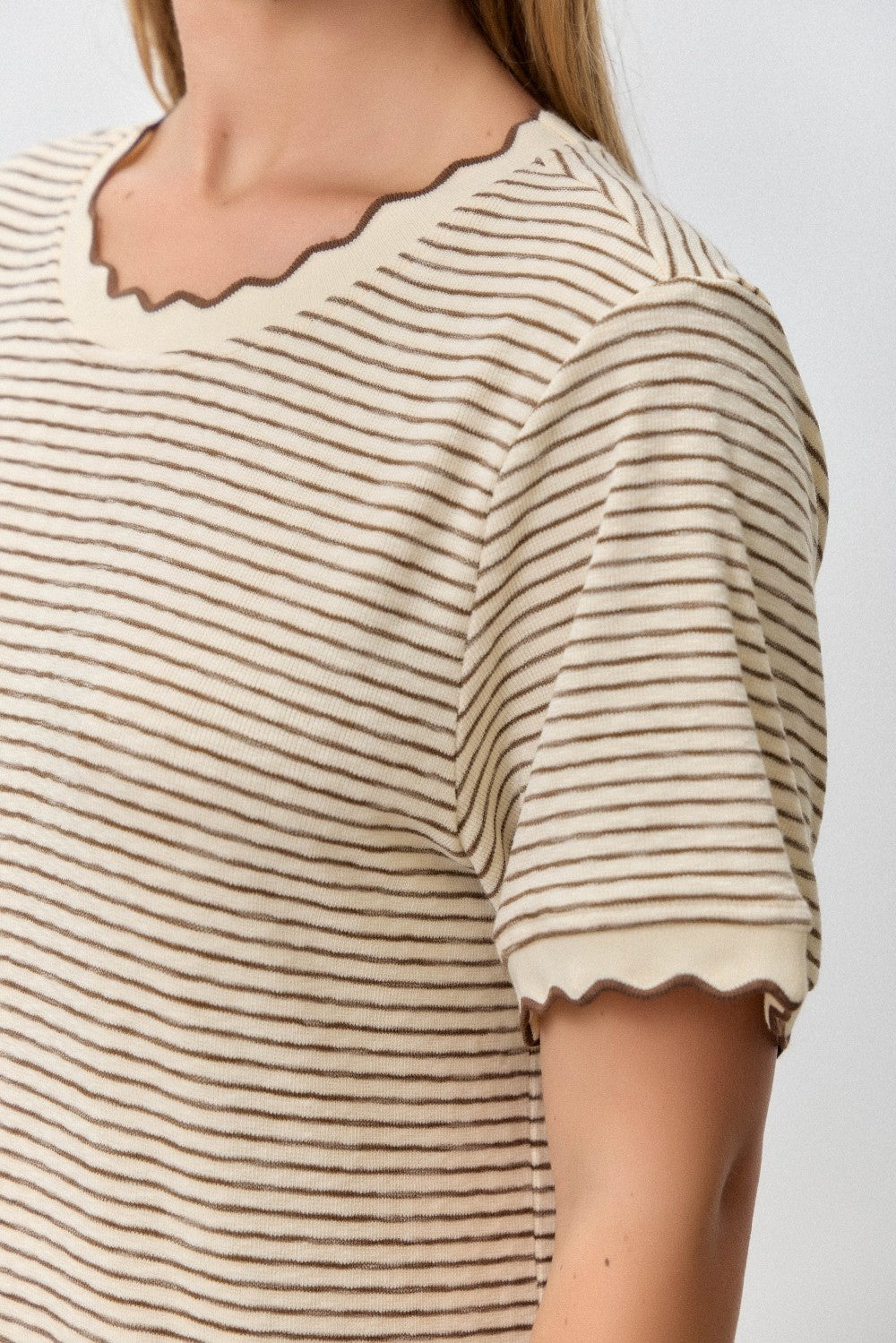 woman wearing a cream and brown striped t-shirt with scalloped edges on the sleeves and neckline