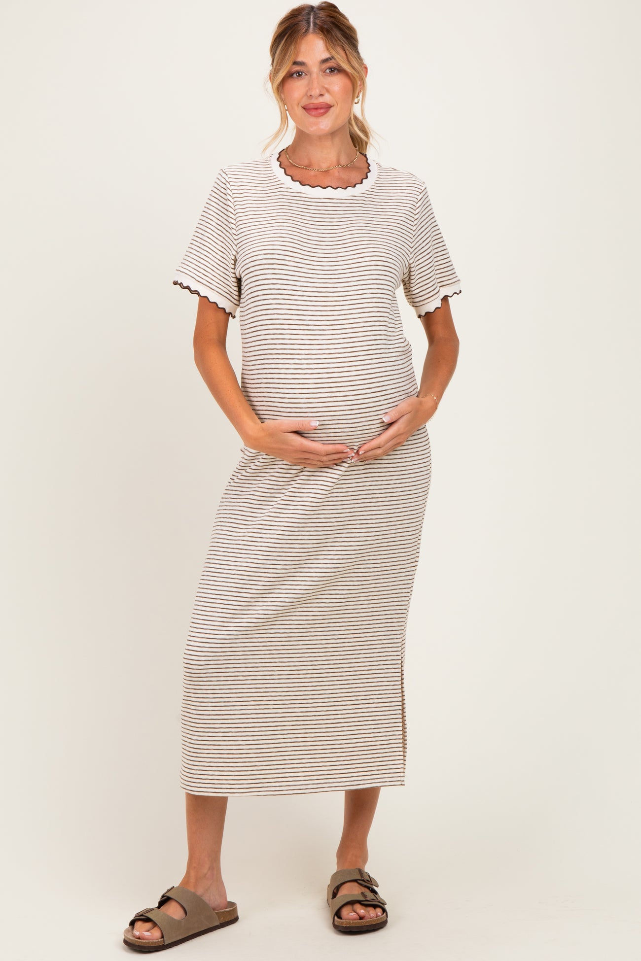 woman wearing a striped beige and brown maternity dress, gently cradling her baby bump