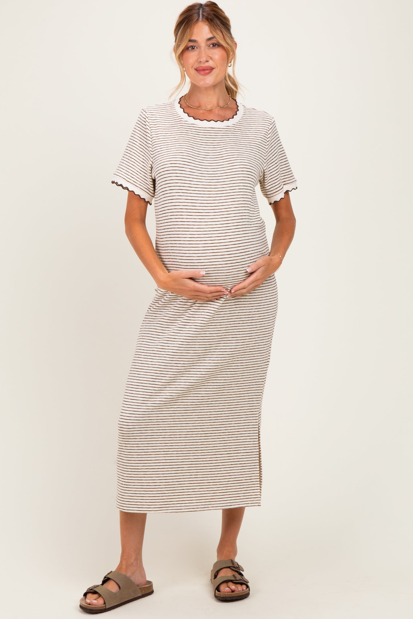 woman wearing a striped beige and brown maternity dress, gently cradling her baby bump