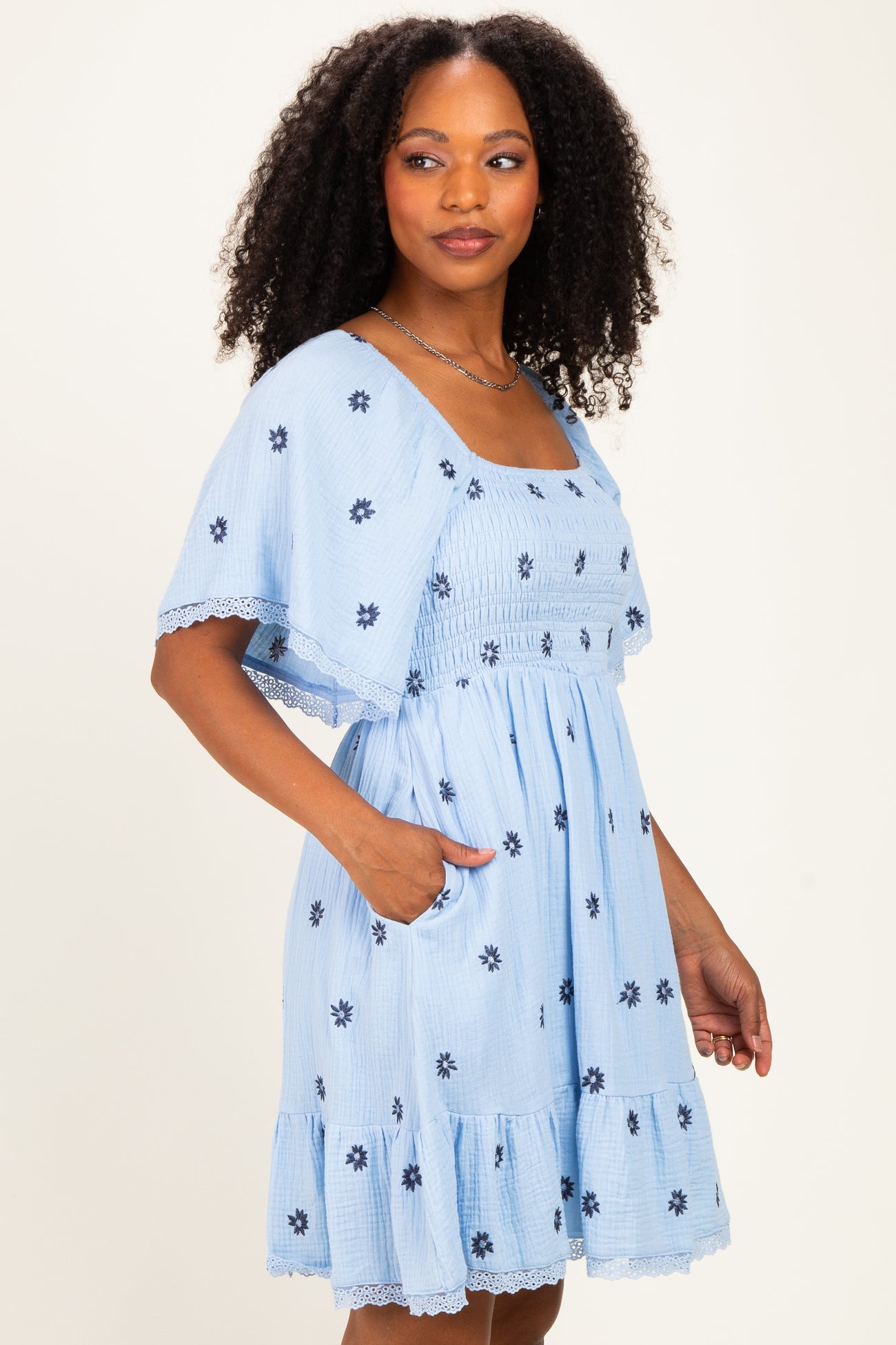 woman wearing a light blue floral embroidered dress with short sleeves and a tiered skirt, featuring pockets