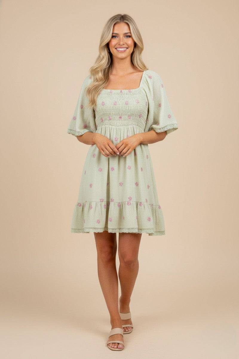 woman wearing a light green short sleeve floral embroidered dress with a smocked bodice and tiered skirt