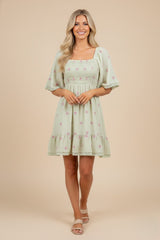 woman wearing a light green short sleeve floral embroidered dress with a smocked bodice and tiered skirt