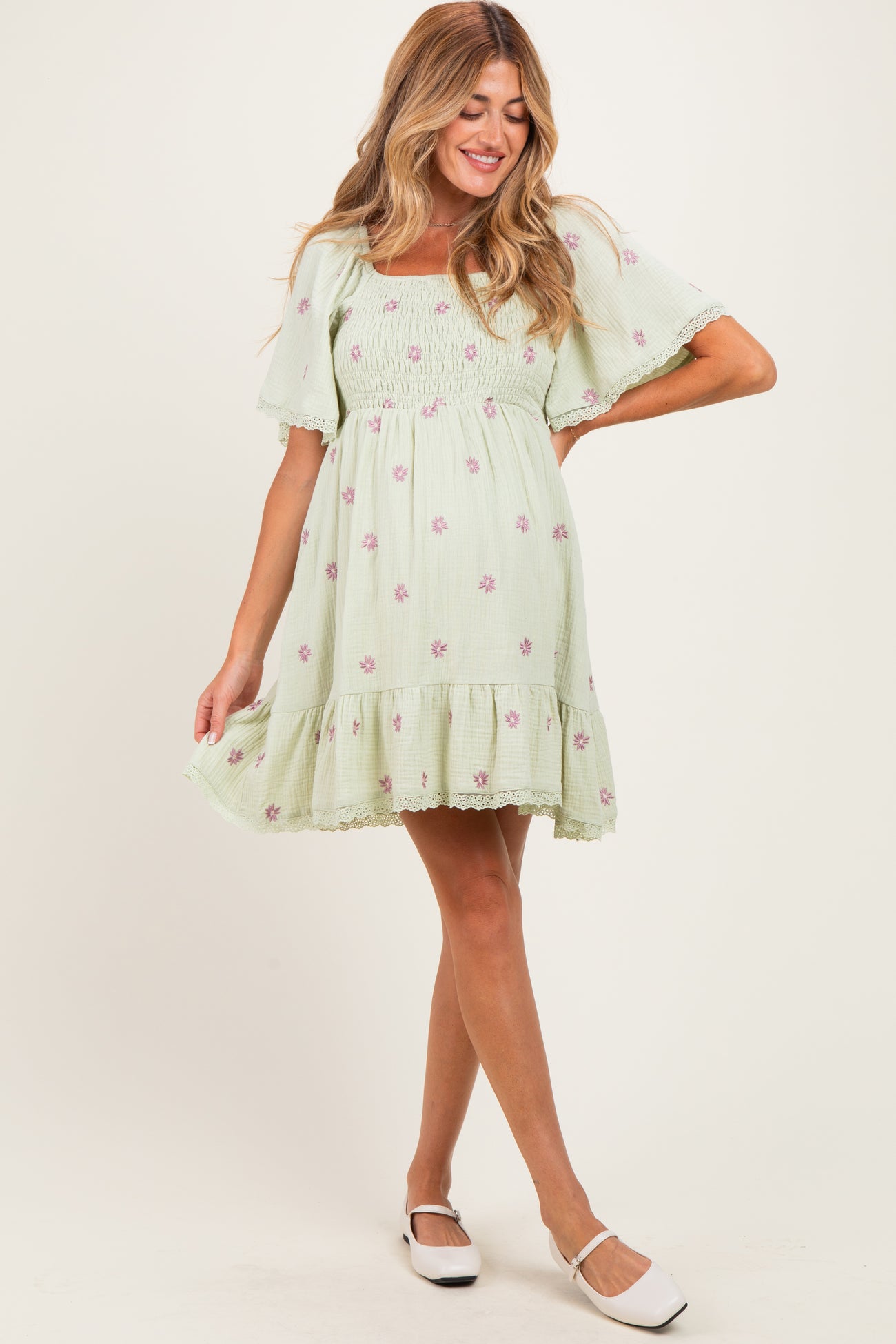 woman wearing a light green floral maternity dress with short sleeves and a smocked bodice, smiling and posing.