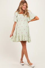 woman wearing a light green floral maternity dress with short sleeves and a smocked bodice, smiling and posing.