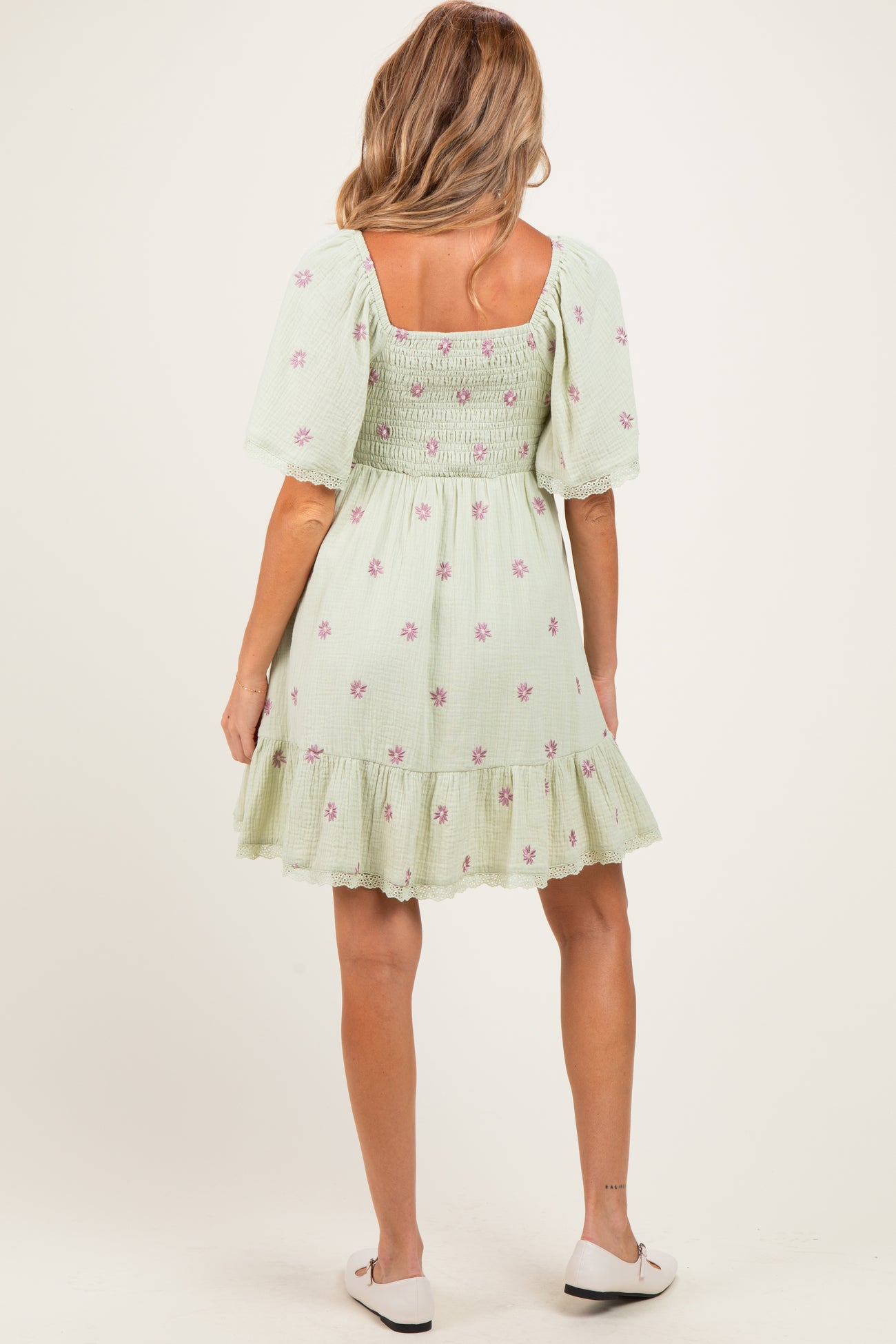 woman wearing a light green floral maternity dress with smocked bodice and puff sleeves, showing off a baby bump
